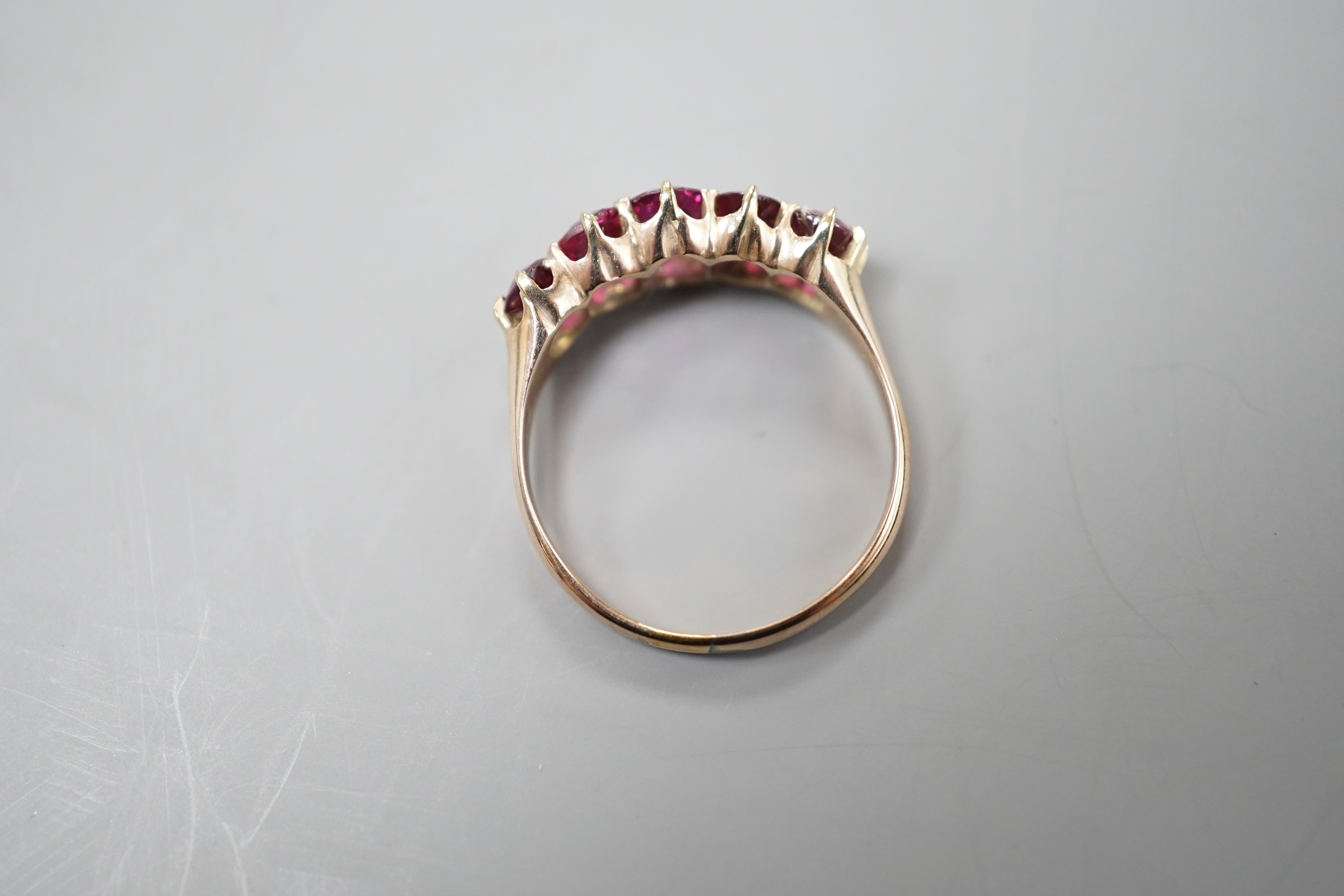 An early 20th century yellow metal and graduated five stone ruby set half hoop ring, size O, gross weight 2.6 grams.